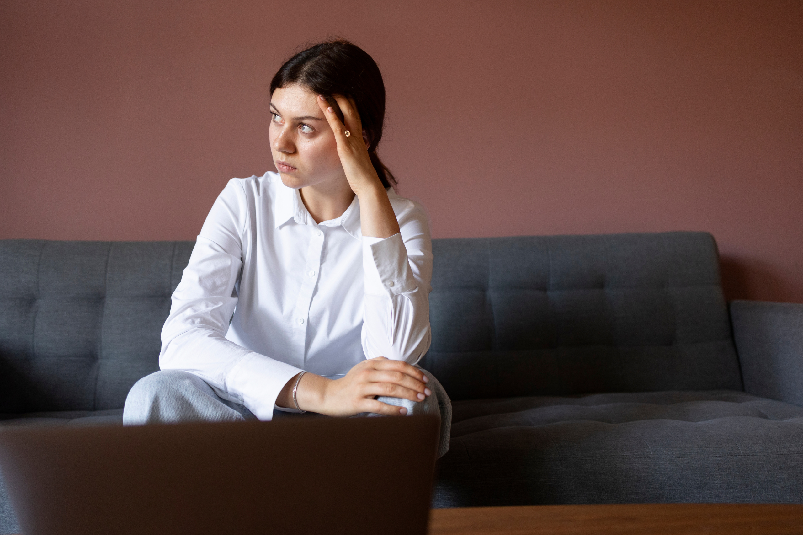 Mujer pensativa sentada en el sofá, representando un estado de desconexión emocional o estrés mental.